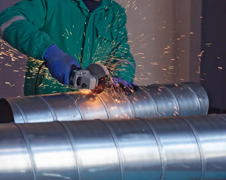 Worker performing custom metal fabrication in Dubai using angle grinder on metal pipes
