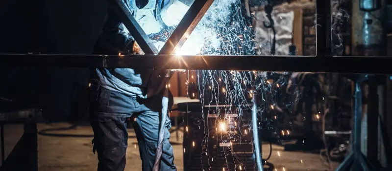 Welder performing custom metal fabrication in Dubai with sparks during steel frame welding